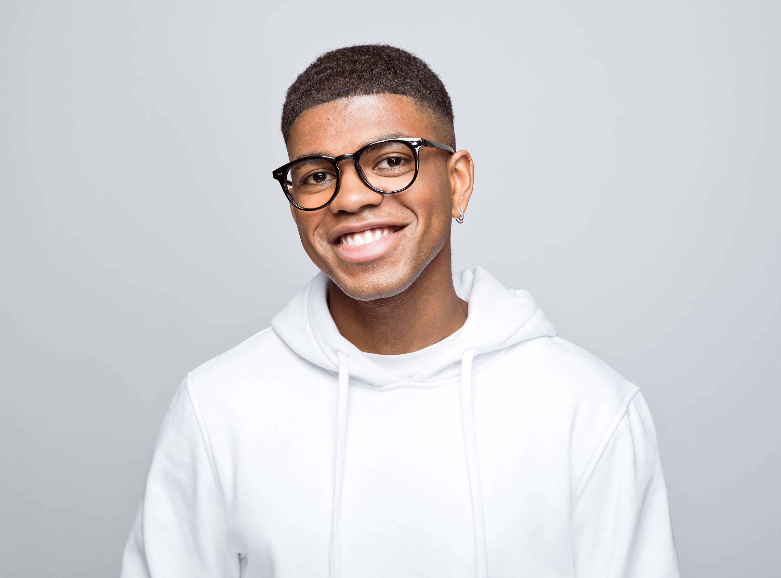 Portrait of a smiling young man with glasses and a white hoodie against a light grey background
