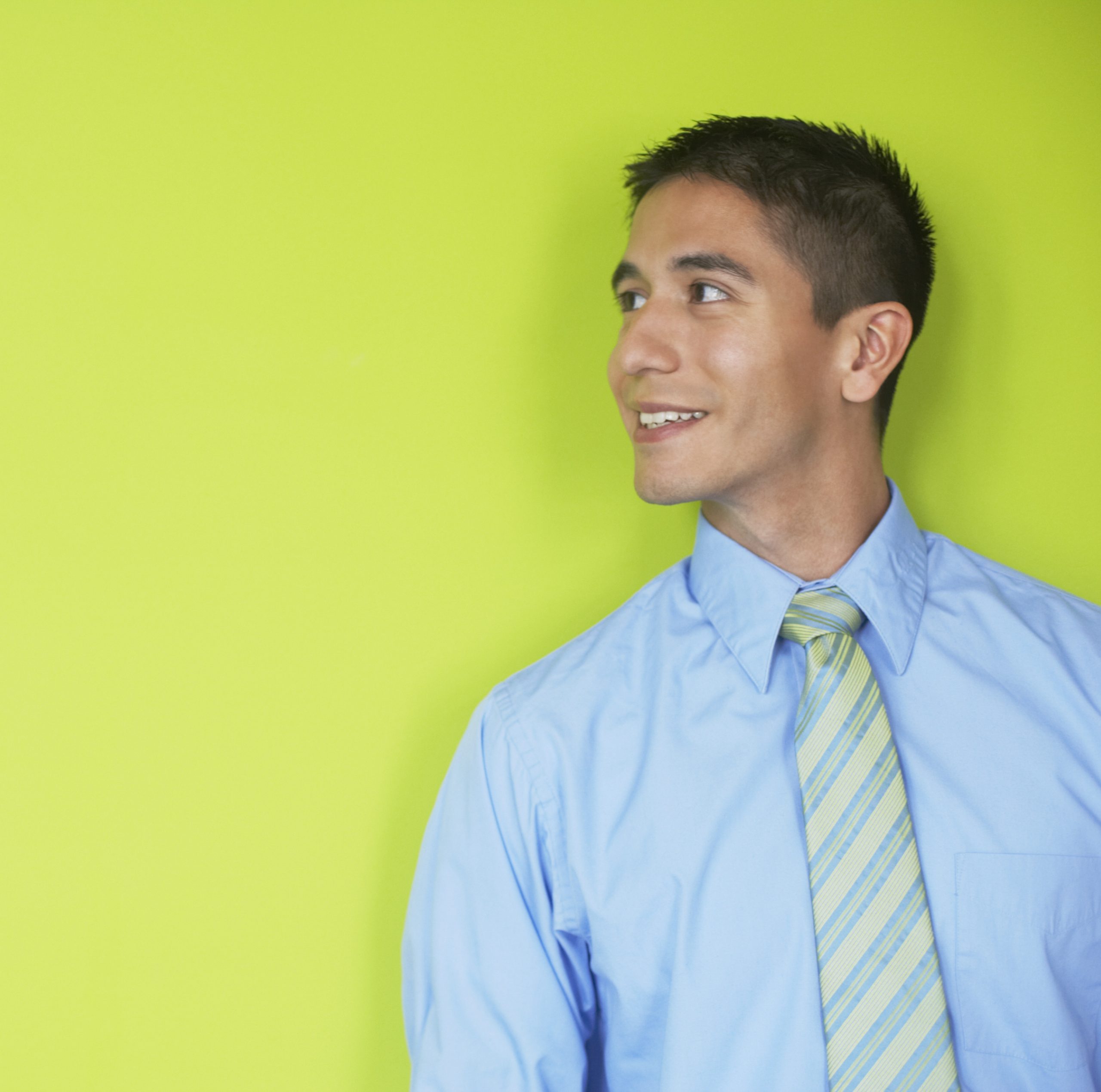 Close-up of a young man standing and looking sideways against a green wall.