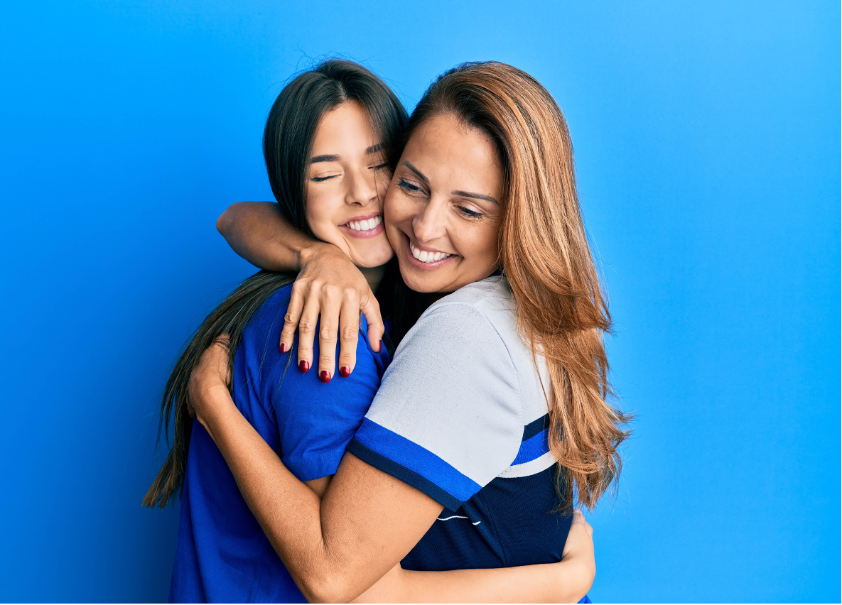 Beautiful mother and daughter smiling happy hugging over isolated blue background.