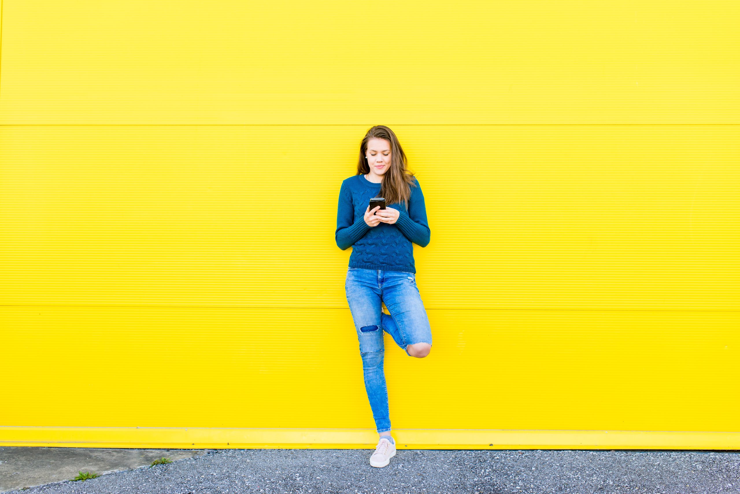 Young woman using a smart phone against vivid yellow background